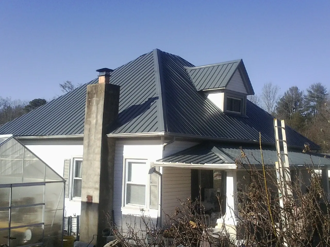 Dark blue standing seam metal roof on a white farmhouse with dormer — Slate & Tile Roof Repair by Roofing Brothers in Knierim