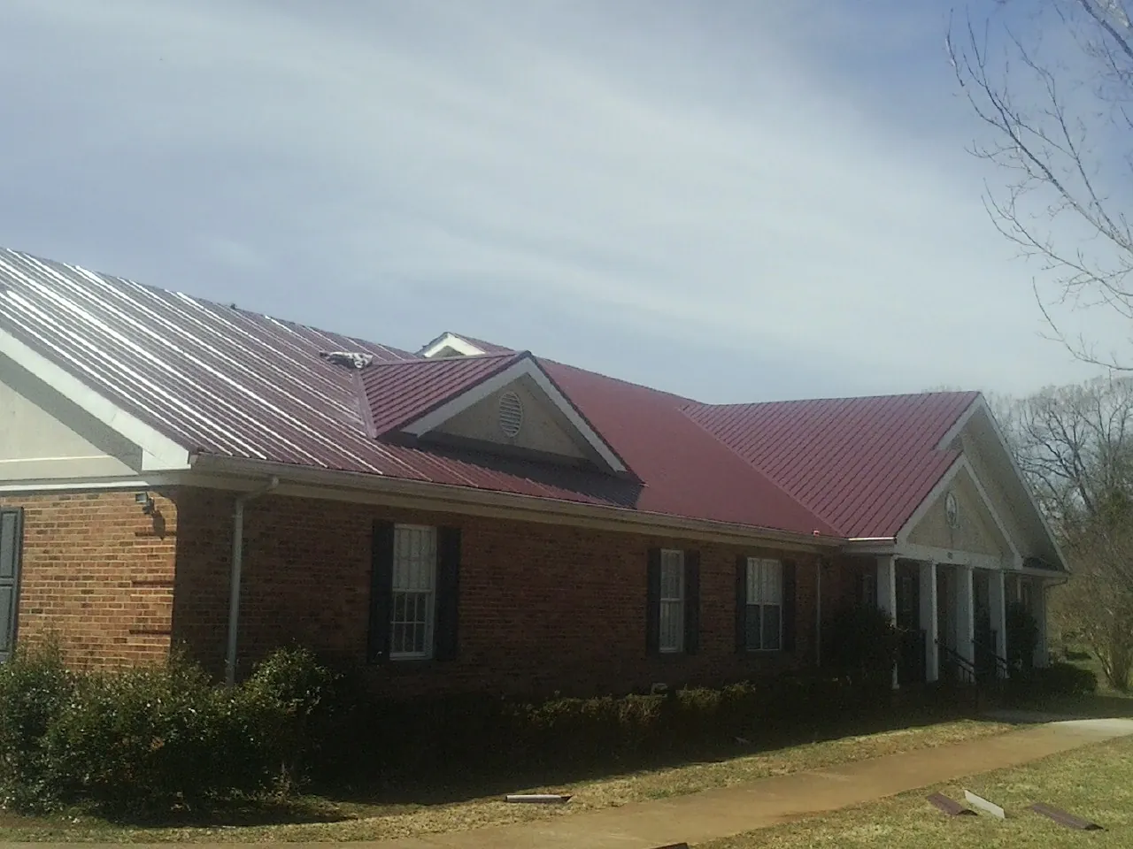 Red metal roof with gabled entries on a long brick building, from a Hail Damage Roof Repair job in Knierim