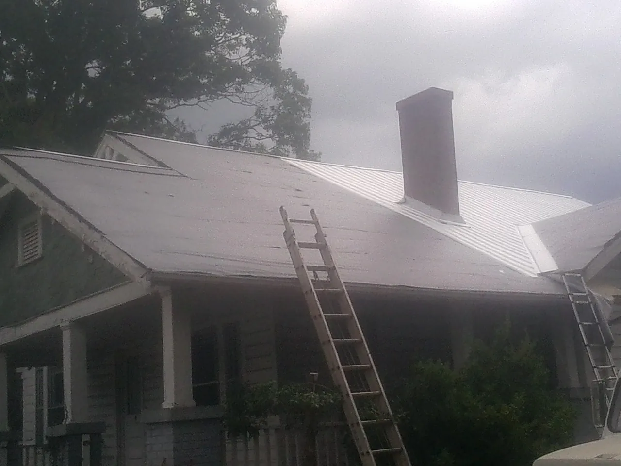 Ladders against a metal roof on an older home with a brick chimney in Knierim