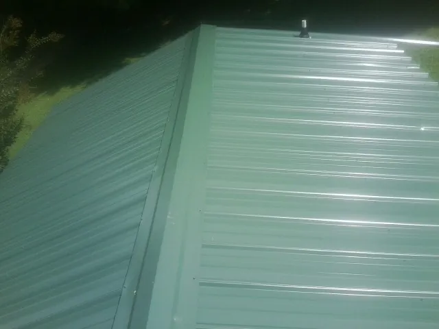 New green metal panels meeting at the ridge of a roof — Flat Roof Repair work by our crew in Knierim