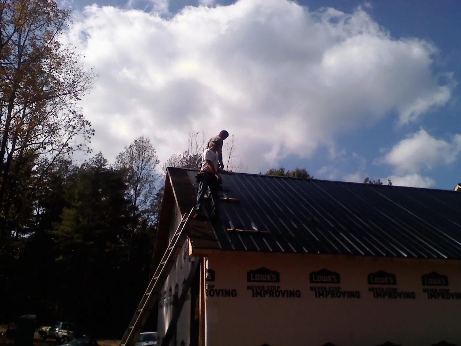 Roofer fastening dark metal panels high against a cloudy sky, from a Roof Inspection job in Knierim