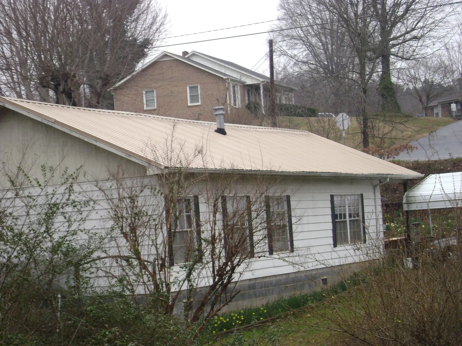 Tan metal roof on a white sided house set into a hillside — Commercial Roofing by Roofing Brothers in Knierim
