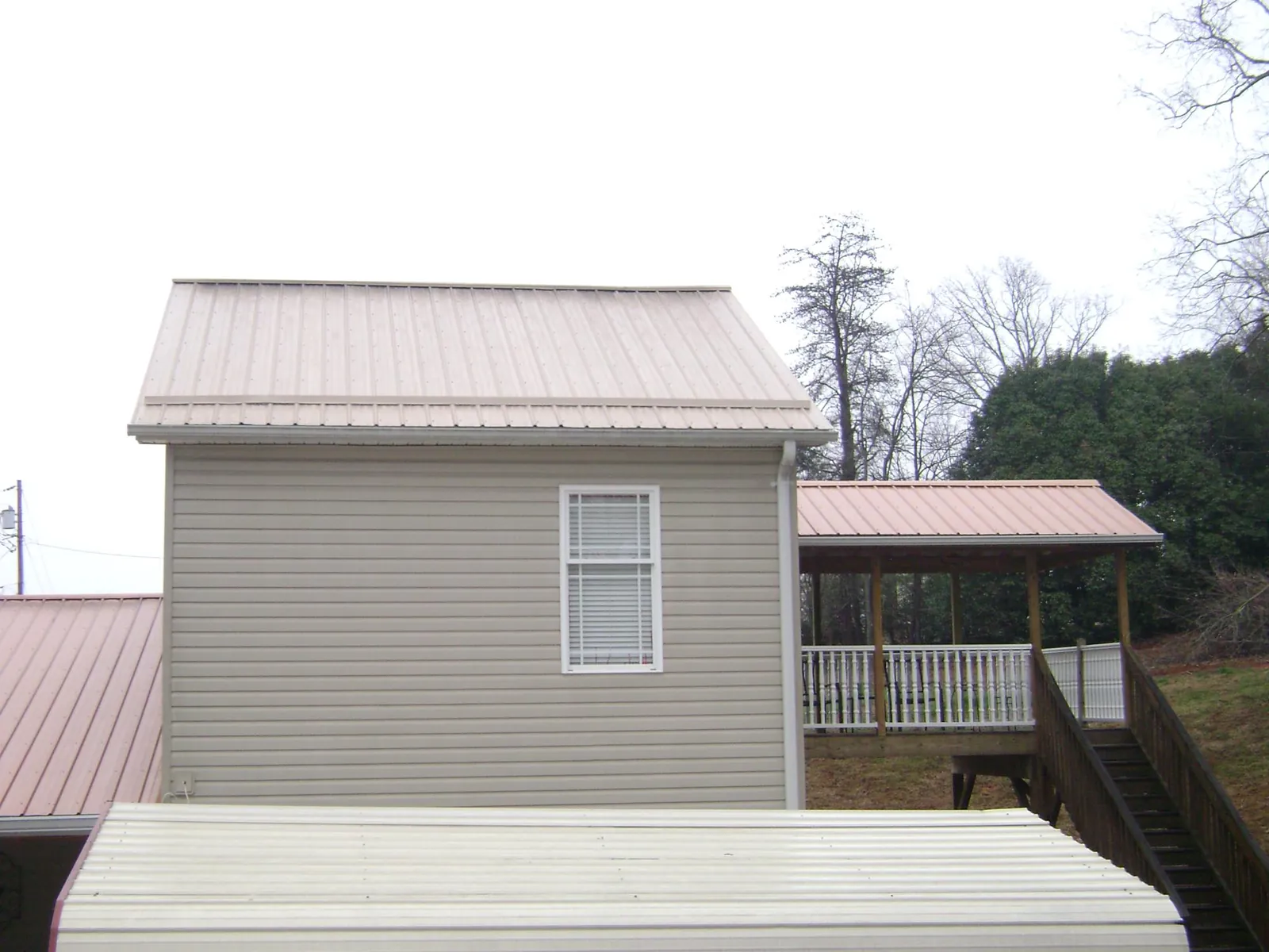 Tan metal roofs on a two story addition and attached porch, from a Roof Replacement job in Knierim